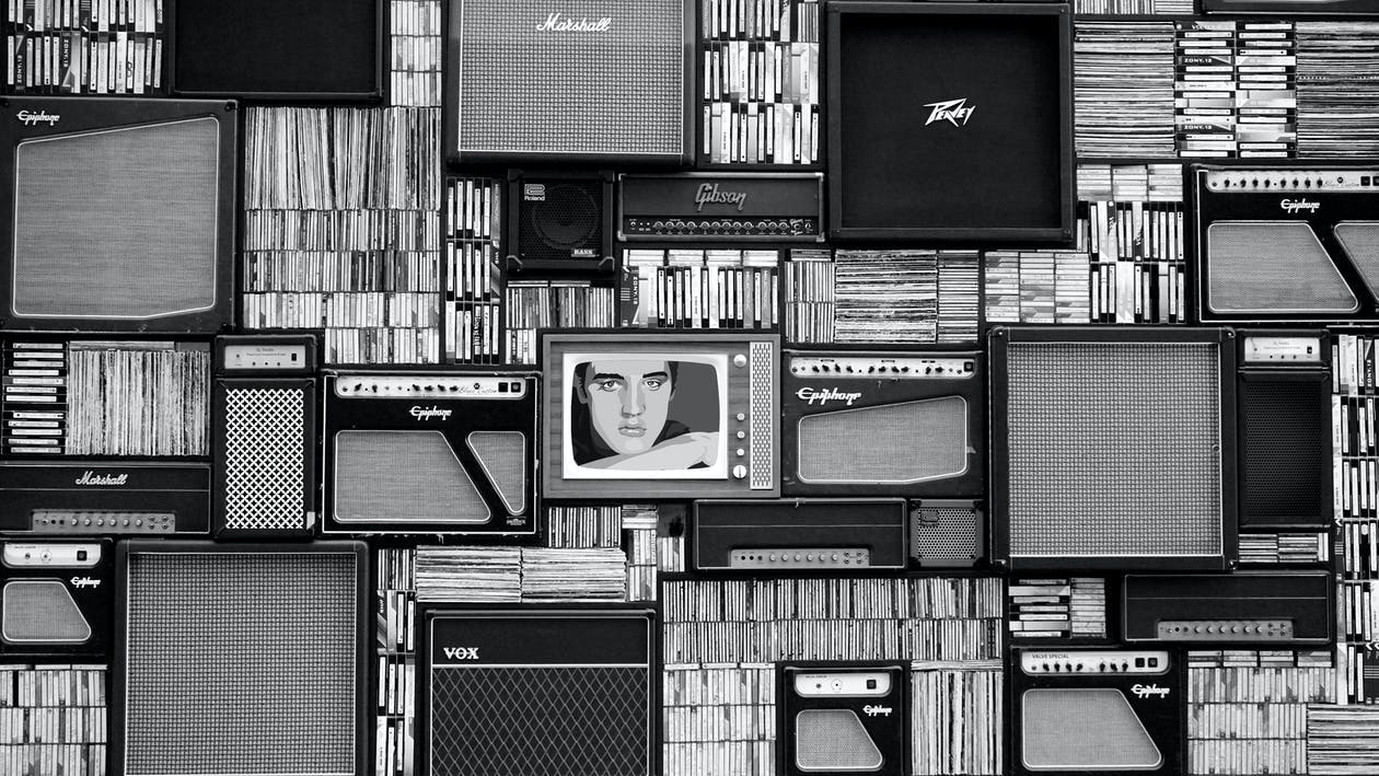 Wall of vintage guitar amplifiers and CD cases with retro TV displaying black and white portrait