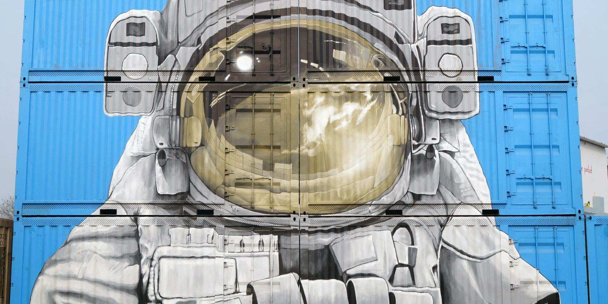 Street art mural of an astronaut helmet painted on blue shipping containers