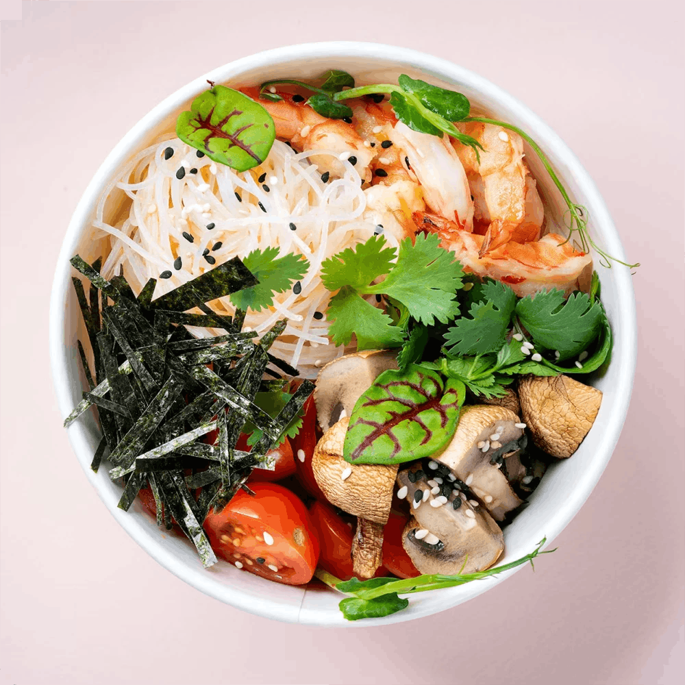 A bowl of rice noodles, shrimp, greens, mushrooms, tomatoes, and strips of seaweed.
