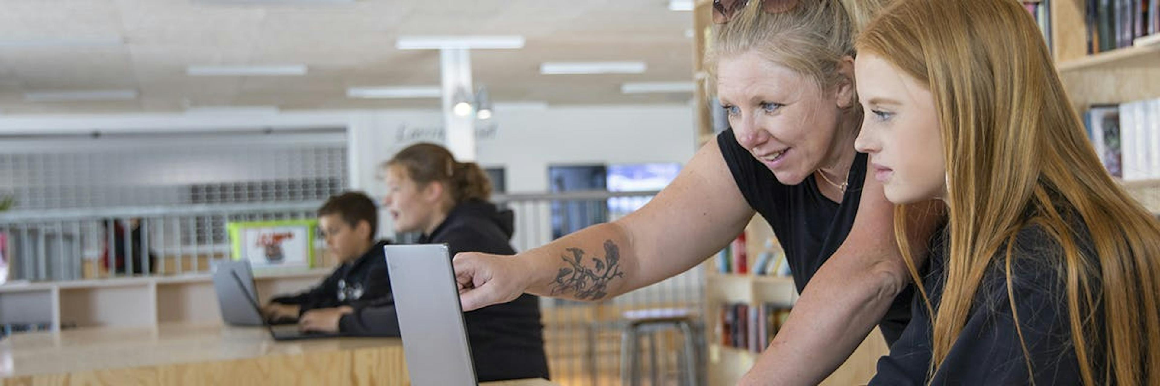 Teacher helping student use laptop