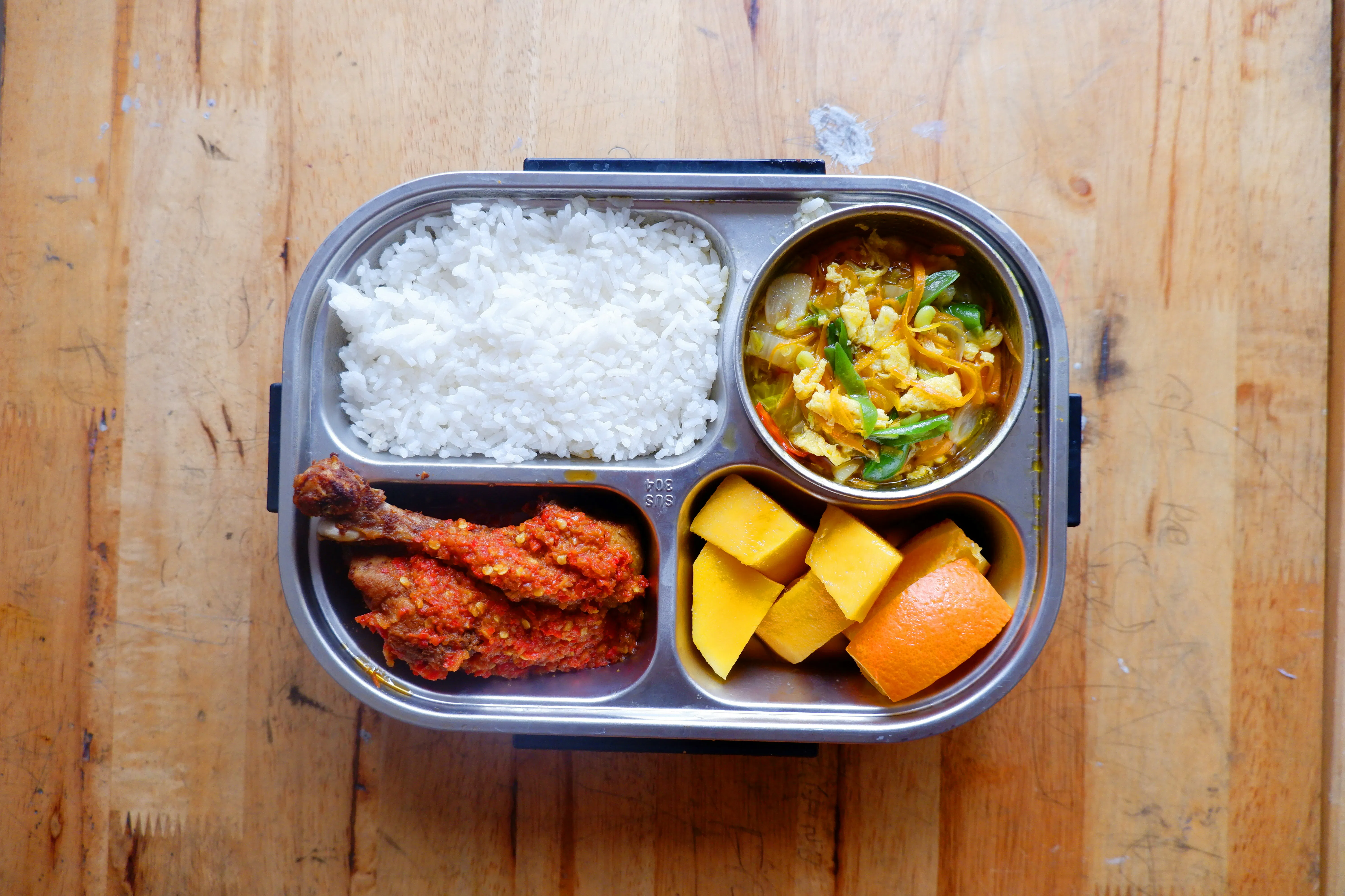 A bento box with rice, fried chicken, kimchi and fruit.