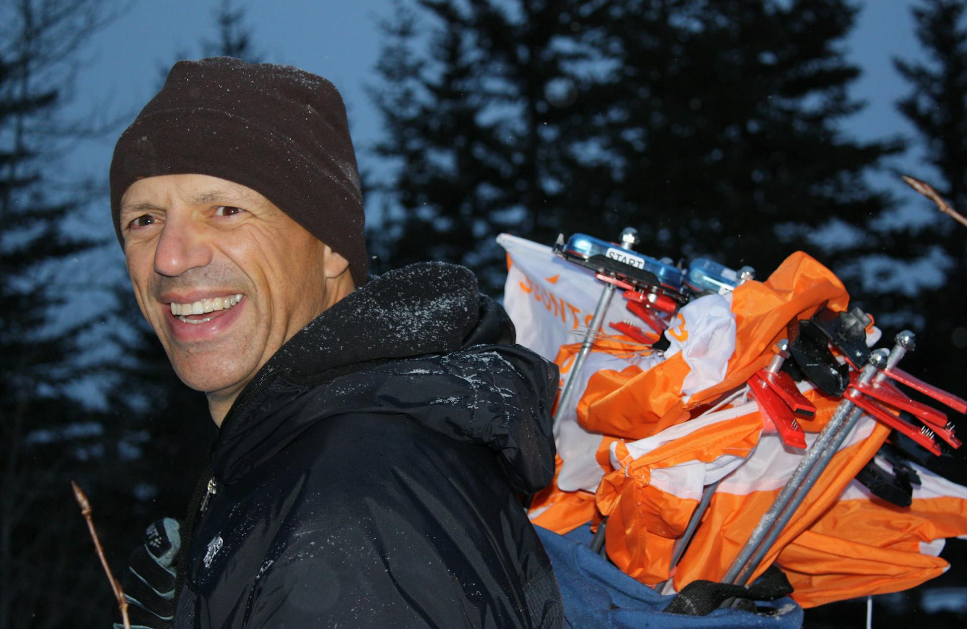 Adrian Zissos smiles at the camera while carrying a backpack full of orienteering controls.