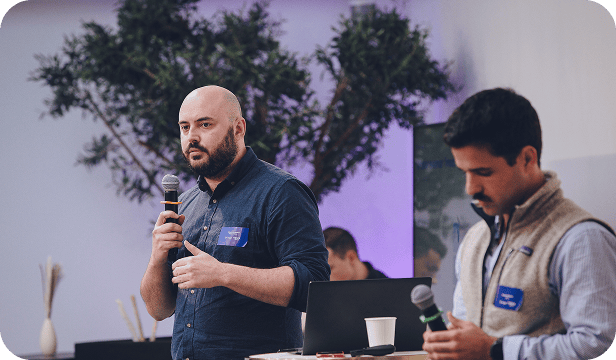 Intervenant tenant un micro à côté d’un autre participant concentré sur ses notes