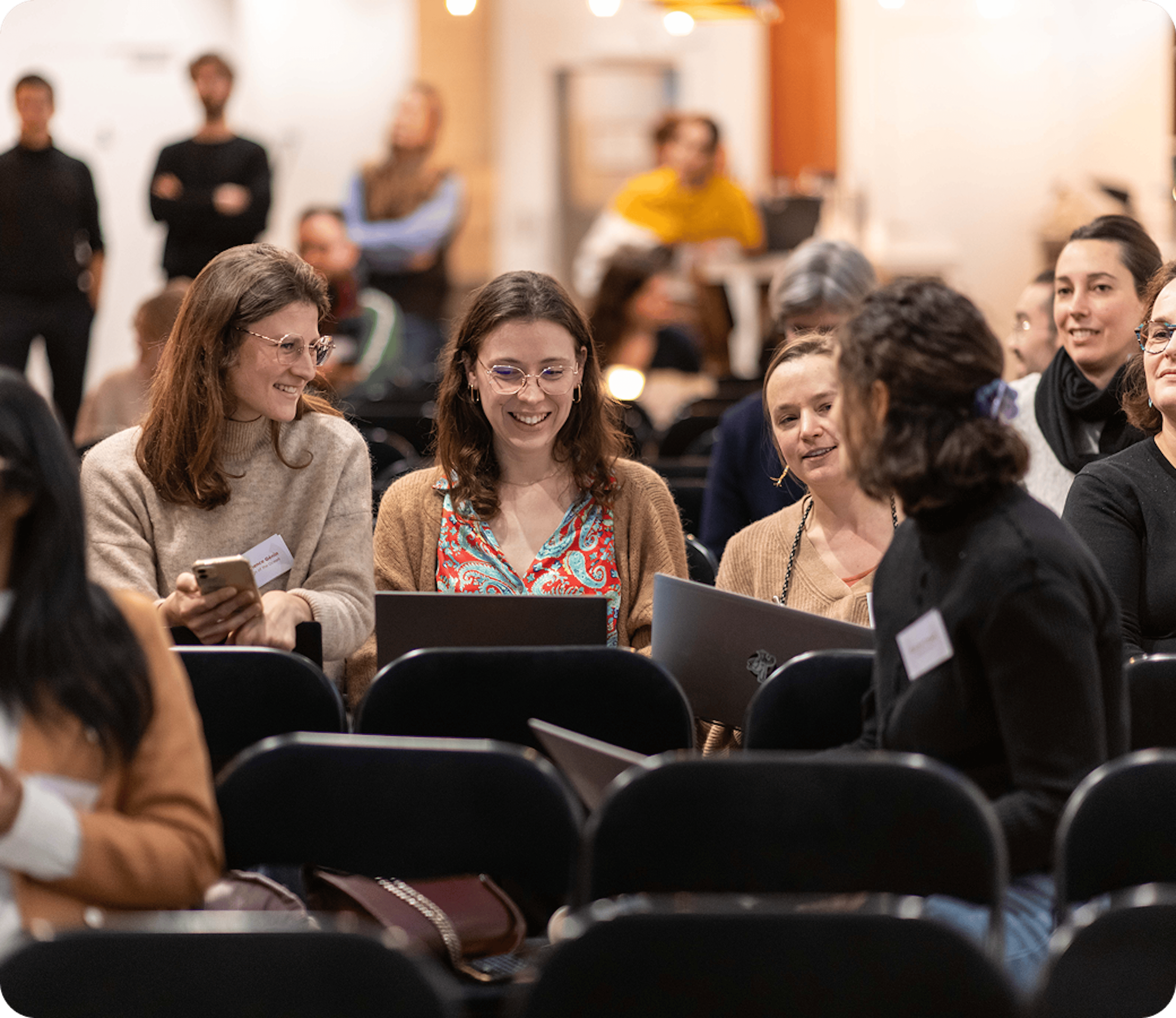 Participants échangeant avant une conférence, ordinateurs portables ouverts.