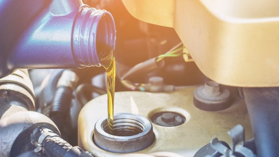 Photographie montrant un bidon d'huile de moteur en train d'être versé dans le réservoir d'huile d'une automobile.