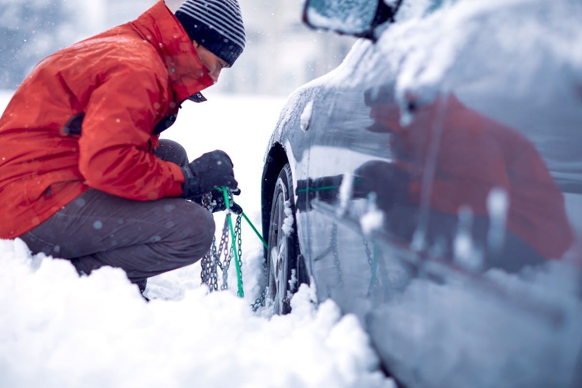 Conducteur installant des chaines a neige sur sa voiture