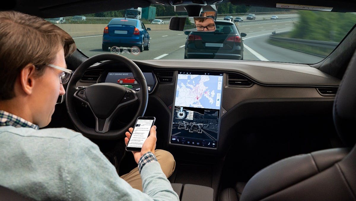 Conducteur d'un voiture a conduite automatisee tenant son smartphone a la main