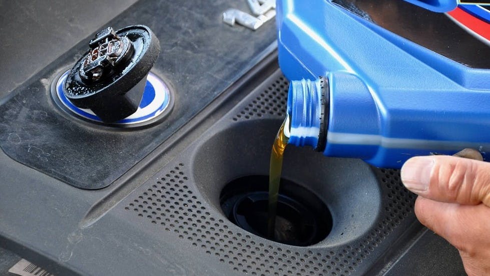 Garagiste versant de l'huile de vidange dans un moteur