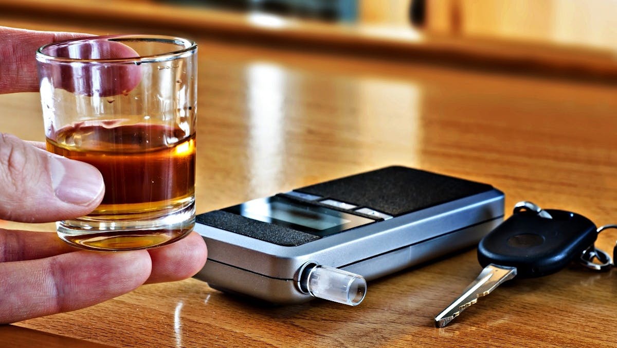 Conducteur tenant un verre d'alcool devant un ethylotest electronique