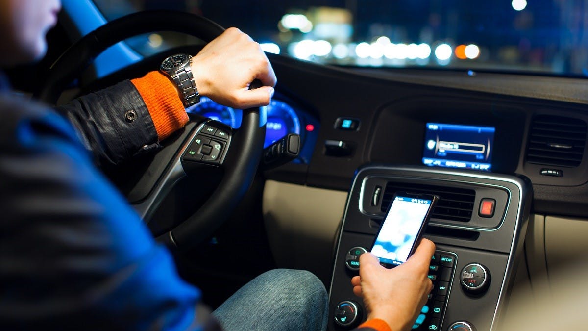 Automobiliste conduisant de nuit avec un smartphone en main
