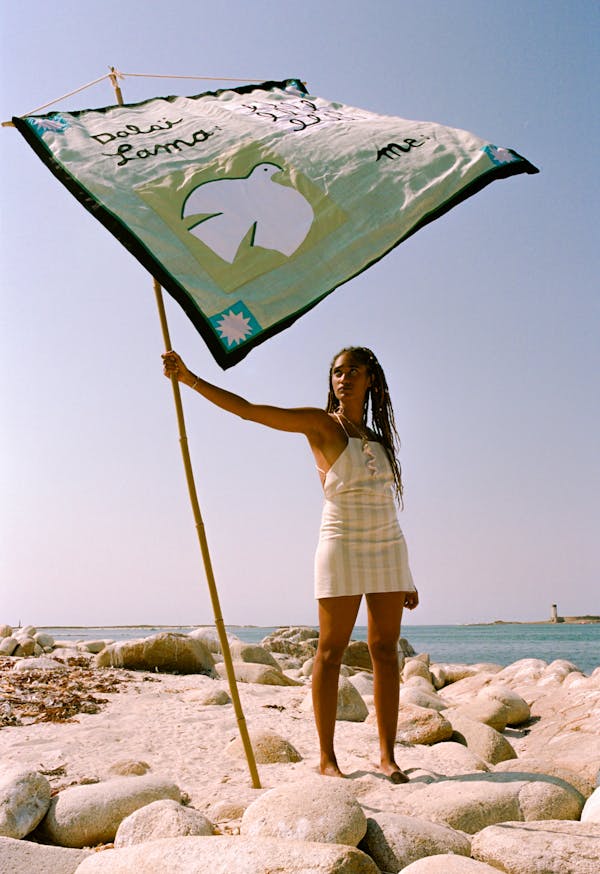 A model stands on the beach holding a Pangea flag, which a 'banner' and represents the thoughts of the Pangea utopia.  | © Pangea 2023
