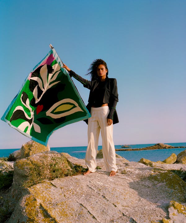 A model stands on a rock on the beach, holding a Pangea flag 'banner'.  | © Pangea 2023