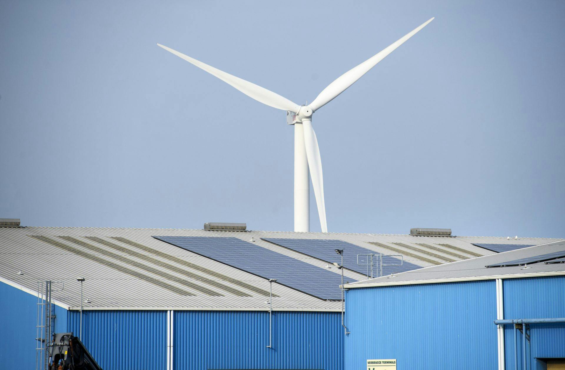 Afbeelding van zonnepanelen op een dak en windmolen op de achtergrond