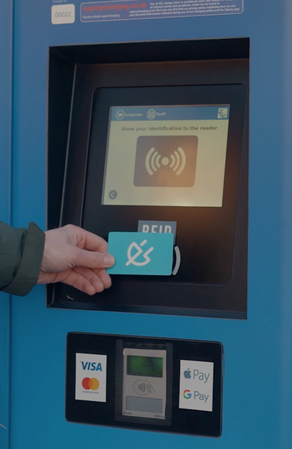 A hand holding a Shell Recharge card to the RFID reader of an EV charging station