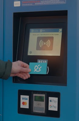 A hand holding a Shell Recharge card to the RFID reader of an EV charging station