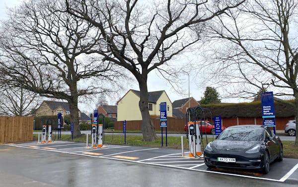 Six high-powered chargers at an Osprey rapid charging hub. A black Tesla is plugged in charging. 
