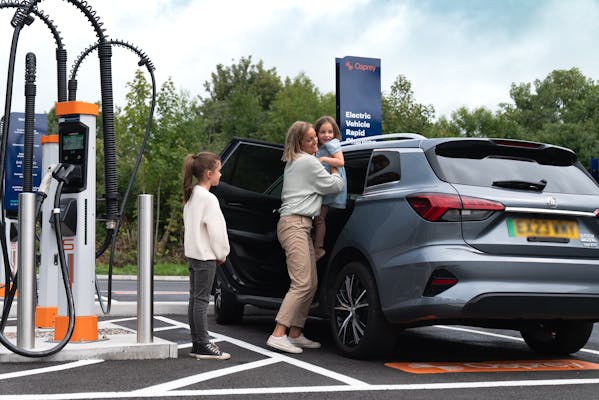 A mother carrying her child out of the electric car at a Osprey EV rapid charger. 