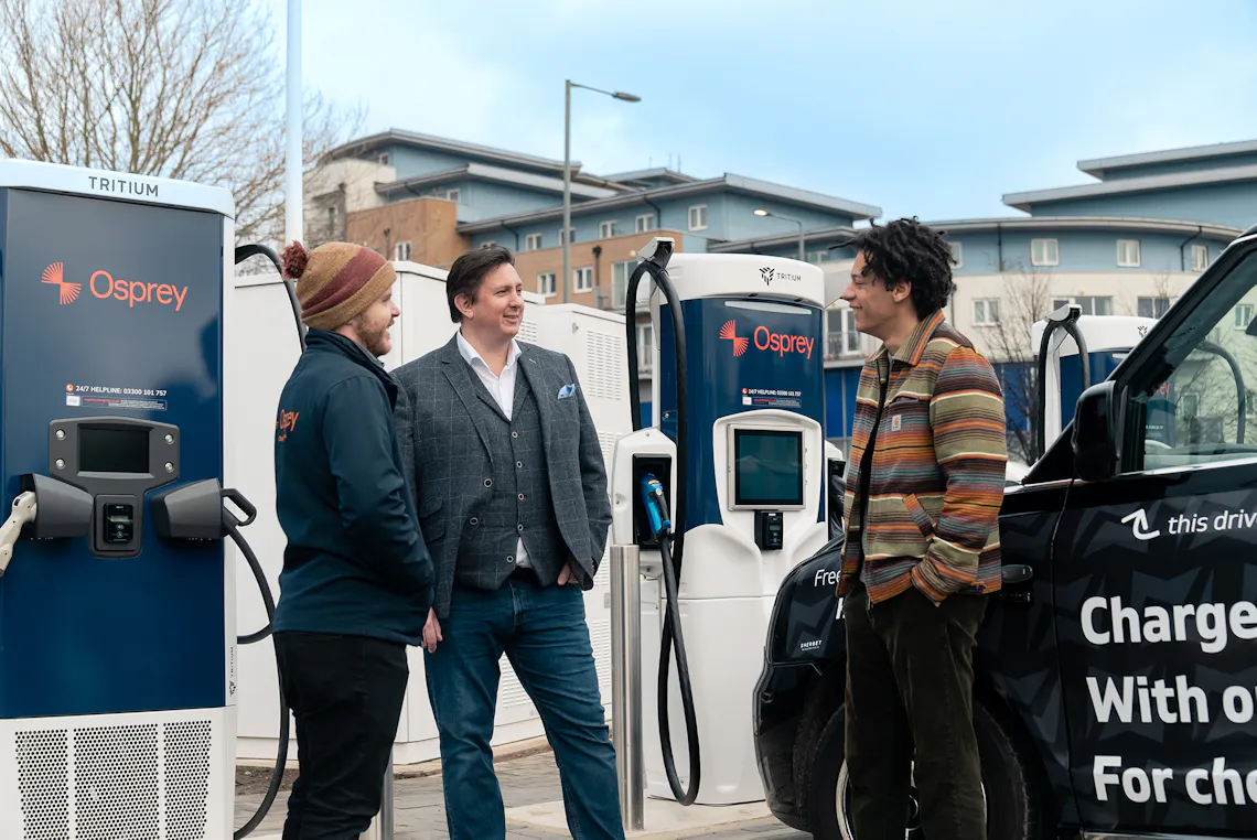 Three men chat in front of an Osprey EV charging hub