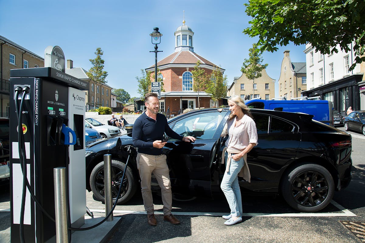 A man and woman chatting next to their Jaguar I-Pace electric vehicle charging at a 50kW Osprey EV charging point