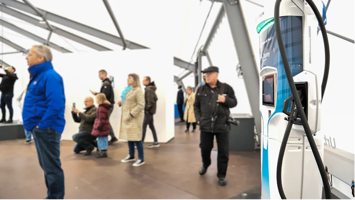 A rapid charger on display in an event hall with people milling about in the background.