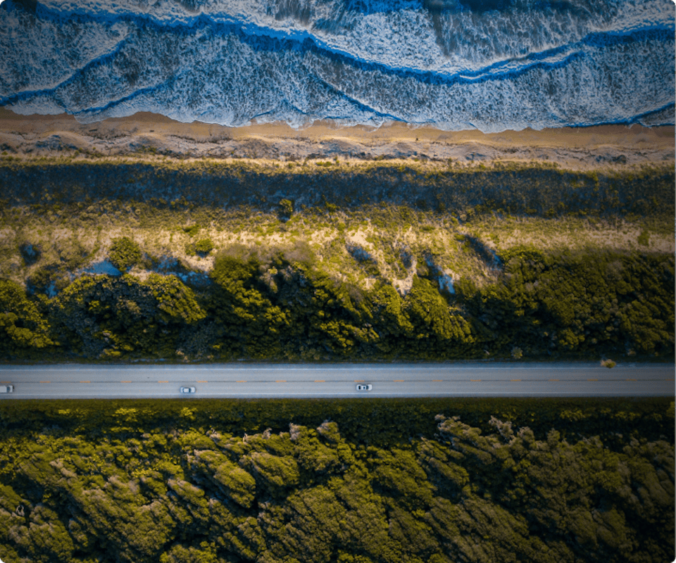 A birds eye view of cars on a straight road cutting through forest and mountains