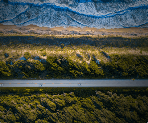A birds eye view of cars on a straight road cutting through forest and mountains