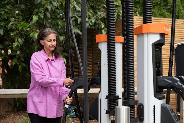 Women wearing a pink shirt at Osprey EV charger holding a charging cable.