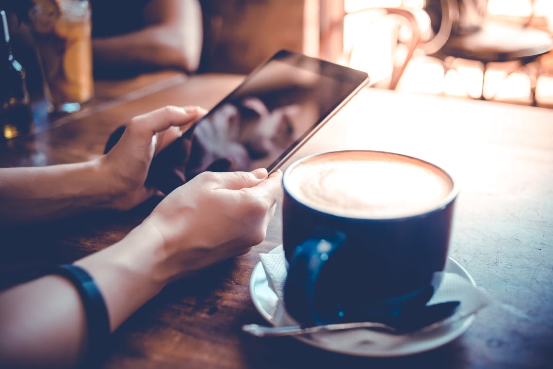 Big cup of coffee and hands holding tablet in cafe. 