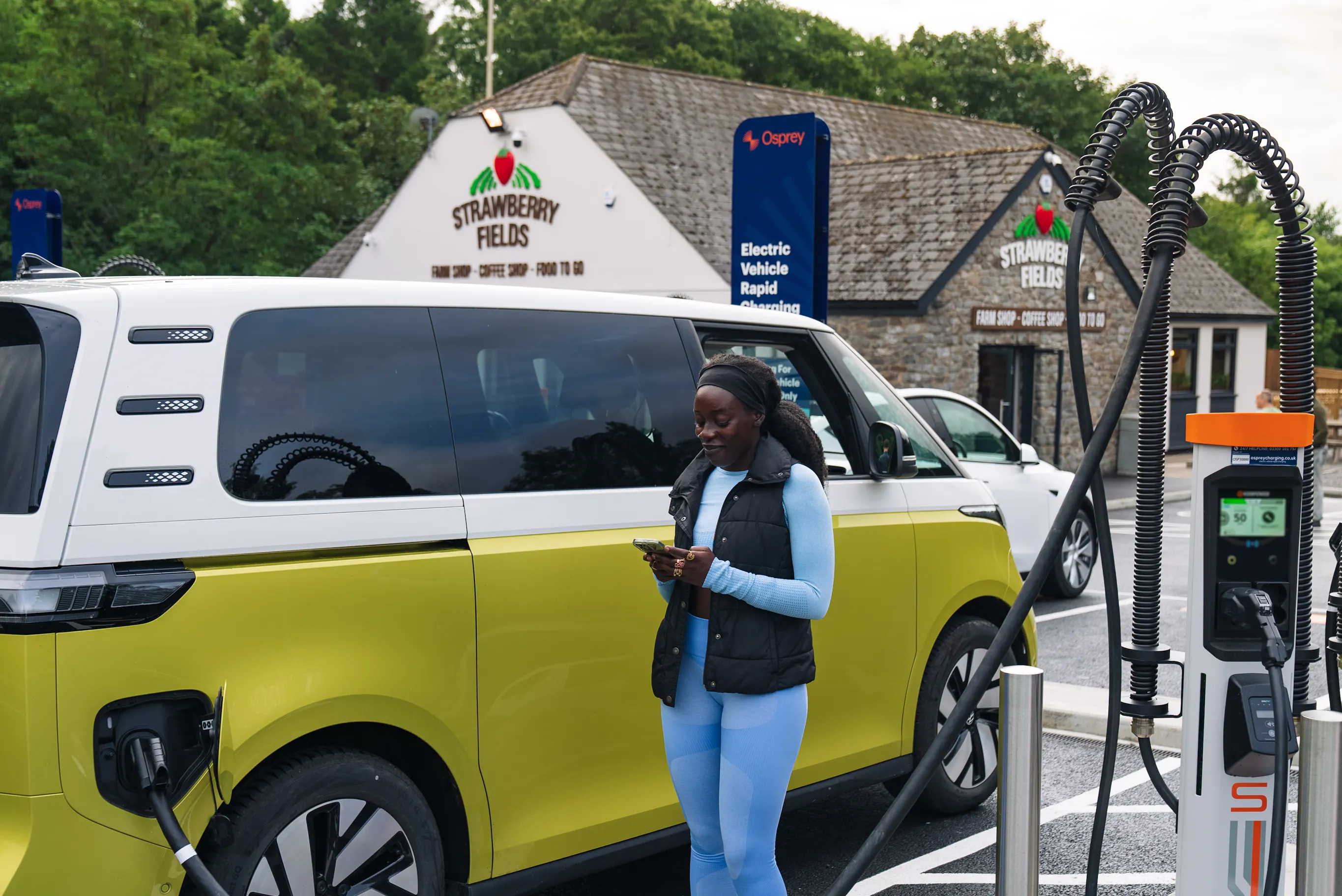 Women standing next to her electric vehicle charging at a Osprey EV rapid charger.