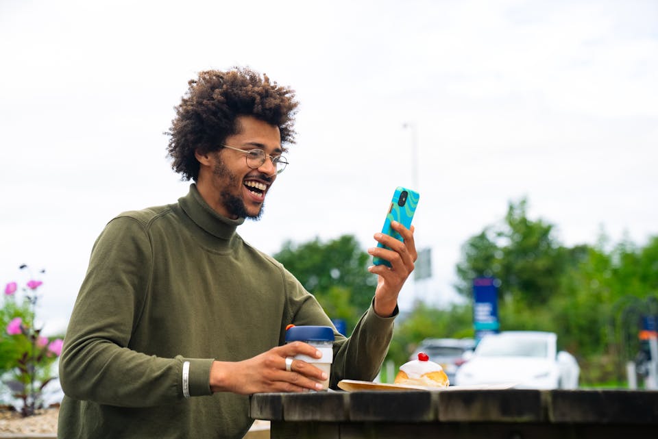 A man with a coffee and chatting on the phone next to an Osprey electric car charging hub.