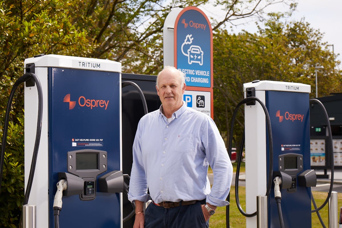 Alex Bamberg stands in front of two Osprey EV charging stations