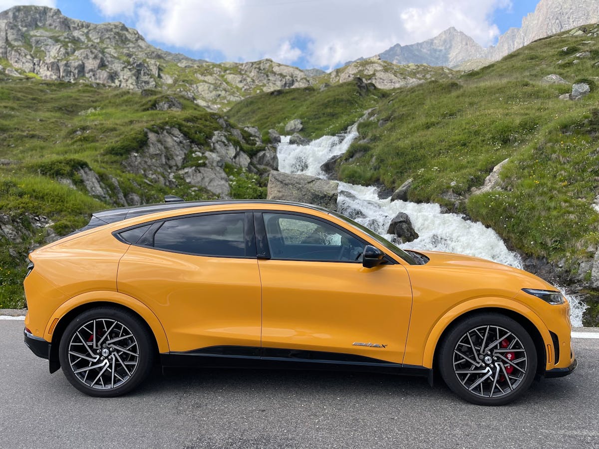 A yellow Mustang Mach-E electric vehicle parked in front of green mountains