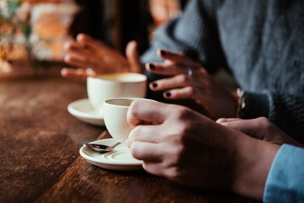 A close up of two coffee cups with a couple of people chatting
