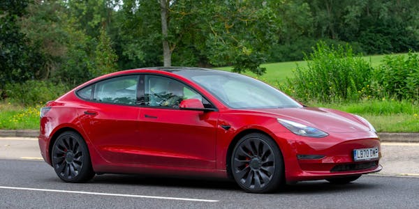 2020 red Tesla Model 3 Performance AWD electric car driving on an English country road.
