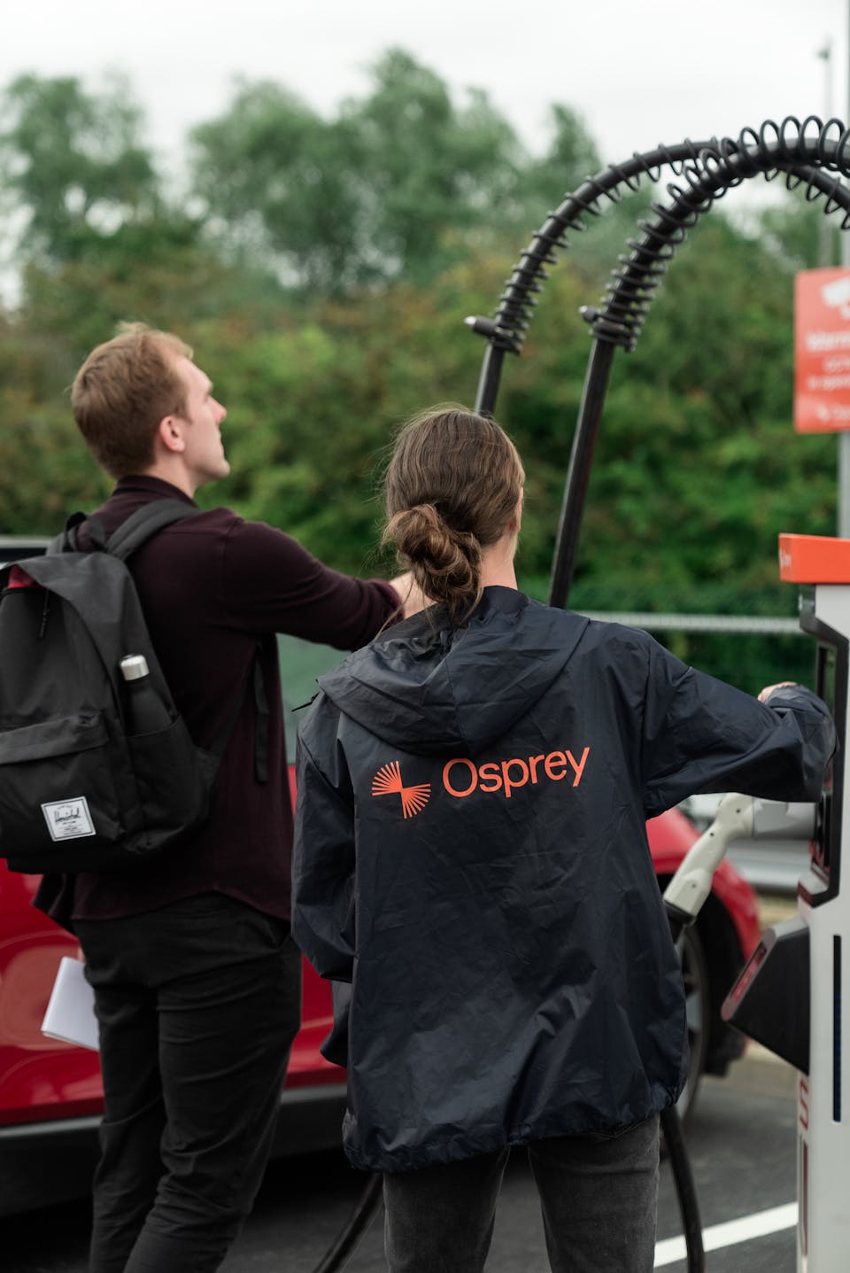 A man wearing a back pack and a woman in an Osprey jacket looking at a rapid charger
