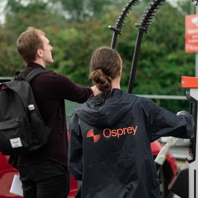 A man wearing a back pack and a woman in an Osprey jacket looking at a rapid charger