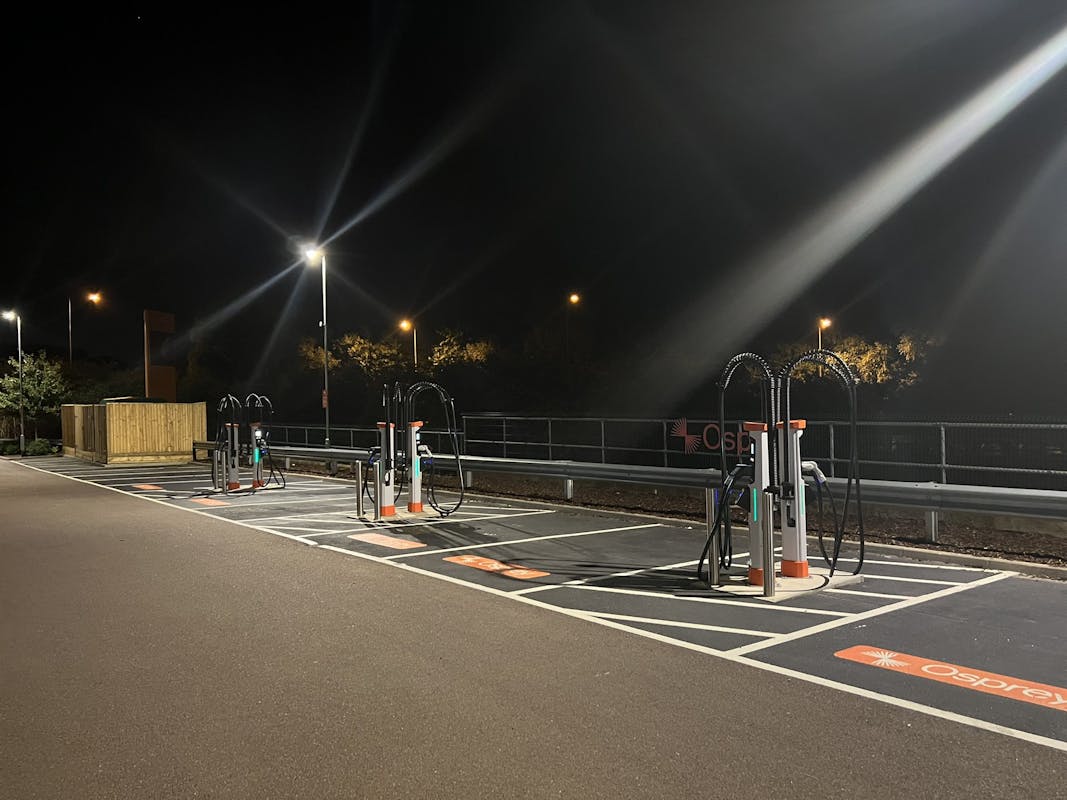 A rapid charging hub at night time with bright overhead lamp posts keeping the site well lit.