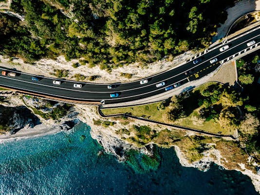 An aerial view busy road wrapping around a mountain with the ocean below it.