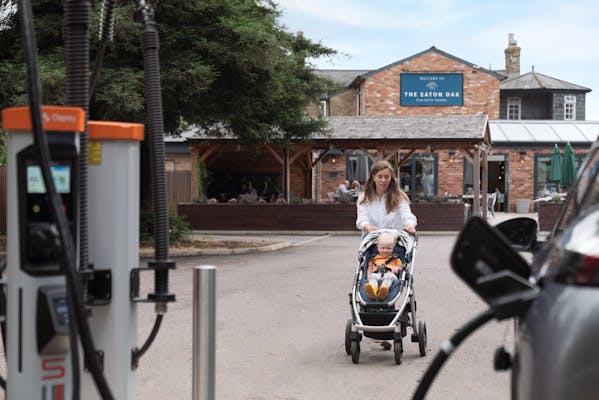 Mother pushing her child in a buggy back to electric car that is charging at a Osprey rapid charger.