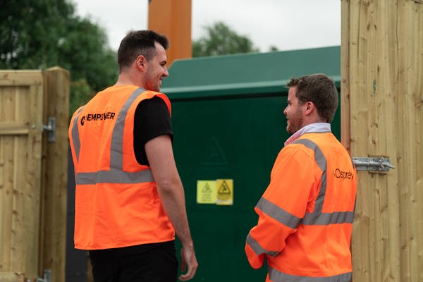 Two men in hi-vis talk in front of a substation