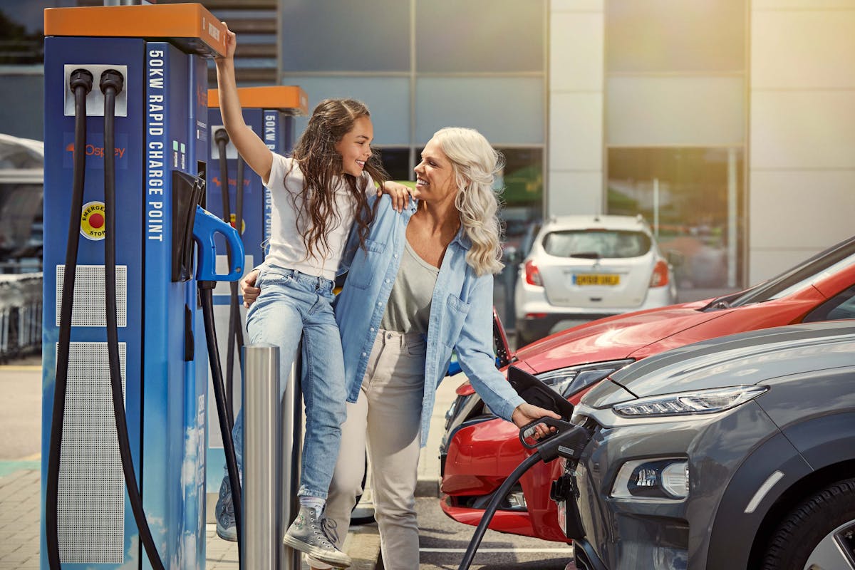 Mum and daughter at a rapid EV charging station charging their car.