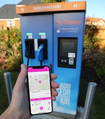 A hand holding a phone with thie Paua EV Charging app open while facing an Osprey charging station