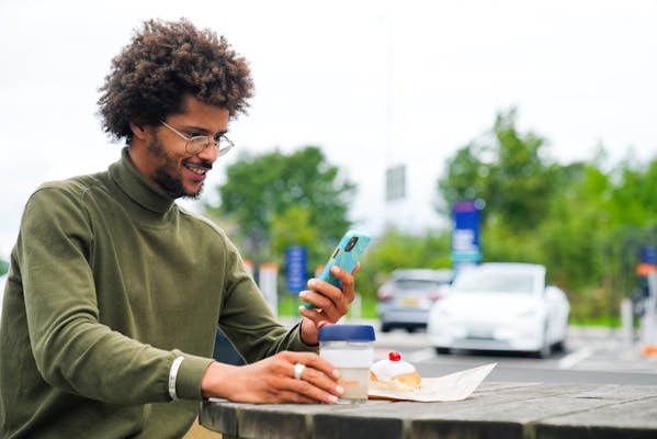 A man with a coffee and chatting on the phone next to an Osprey electric car charging hub.