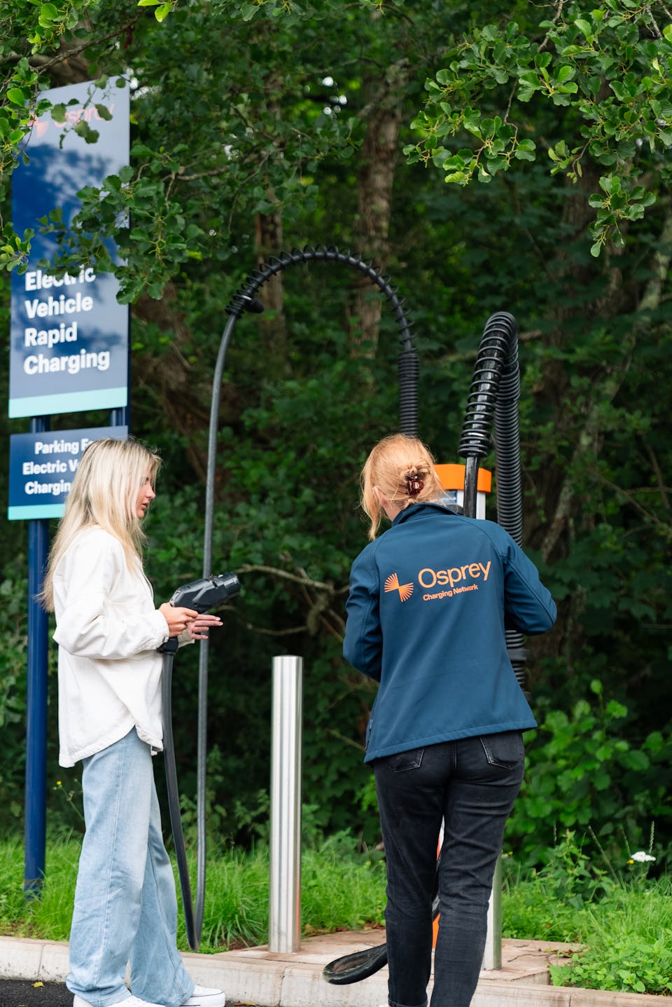 Two women unplugging the Osprey EV rapid charging cables from the charging station.
