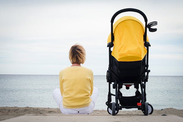 A woman in a yellow jumper sits next to a pram looking at the ocean