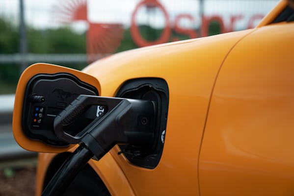 A close up of a rapid CCS connector plugged into an orange car with an Osprey sign behind.