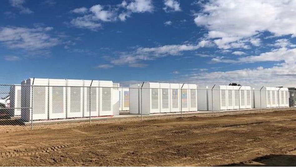 Over 20 large battery power storage units installed in a field.