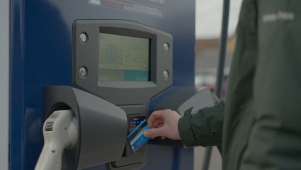 A person holding a bank card to the payment terminal of an Osprey EV charging station 