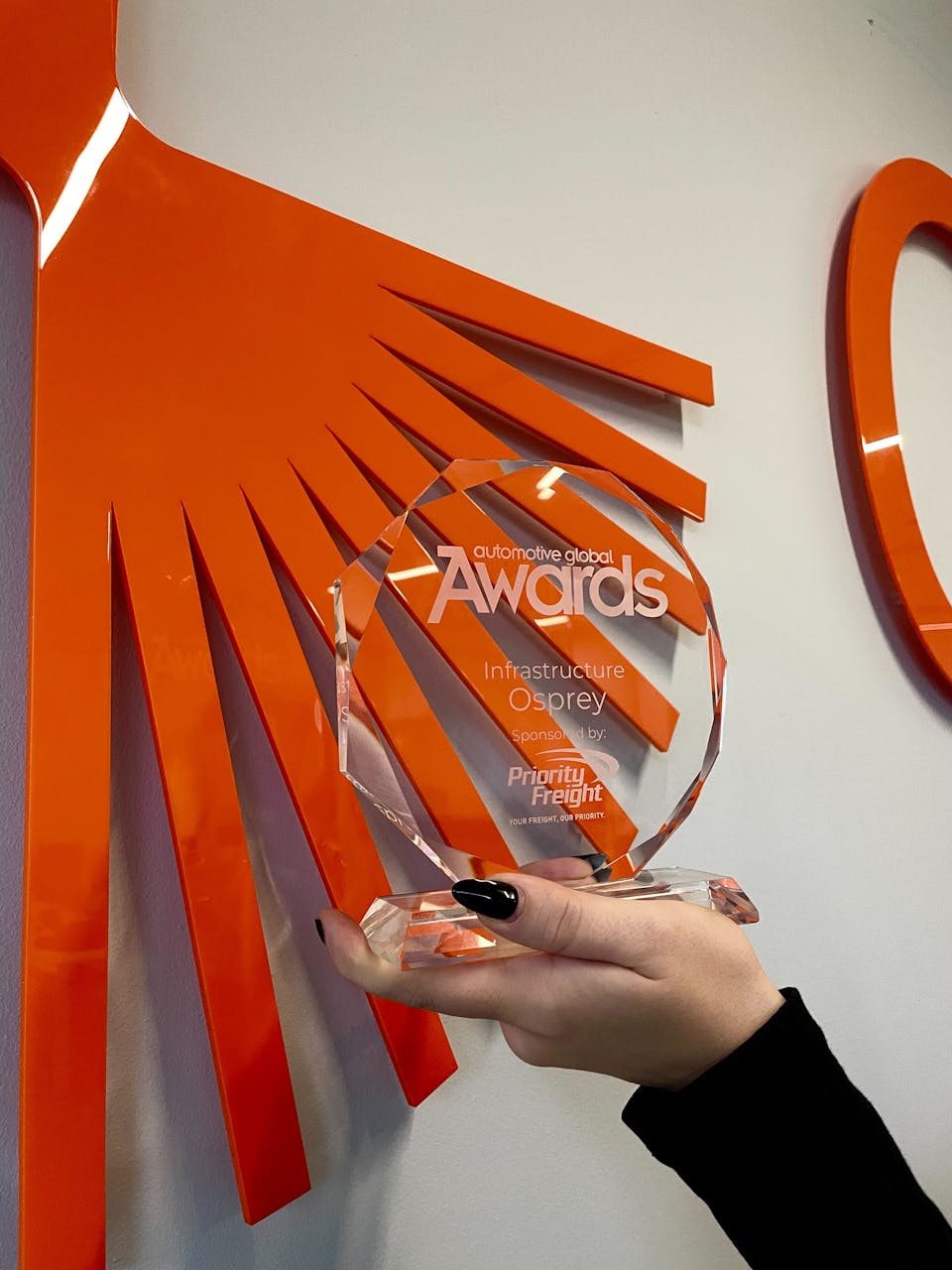 A hand holds a glass award in front of an Osprey sign