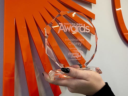 A hand holds a glass award in front of an Osprey sign